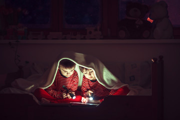 Two sweet boys, reading a book in bed after bedtime, using flash