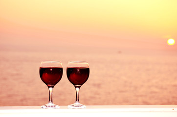 Two red wine glasses in front of the setting sun.Sea background