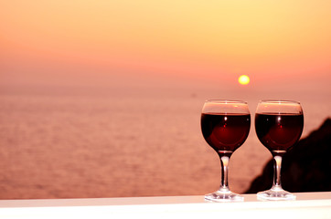 Two red wine glasses in front of the setting sun.Sea background