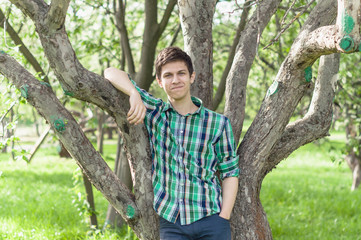 a young man in a plaid green shirt posing near a tree in the summer park