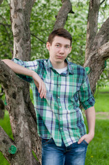 a young man in a plaid green shirt posing in a park in spring