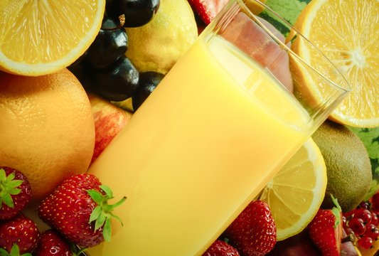 Schr&auml;g stehendes Glas mit Orangensaft gef&uuml;llt , umgeben von Fr&uuml;chten und Obst