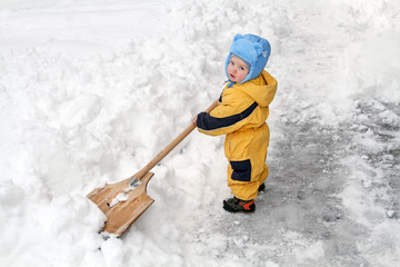 Little boy with big wooden shovel to clear snow. A very snowy wi