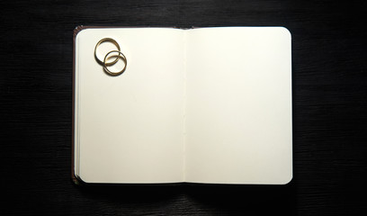 Blank notebook with wedding rings on black background