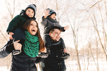 Cute young family with twins and pregnant young mother having fun in winter park on a bright day hugging each other and smiling
