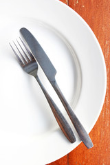 Fork and knife in white plate on wooden table.