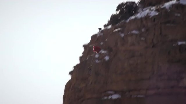 Shot of base jumper flipping with skis and opening parachute.
