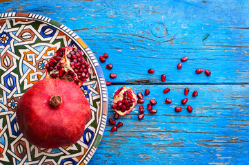 red ripe pomegranate in dish oriental style with copy space on wooden background