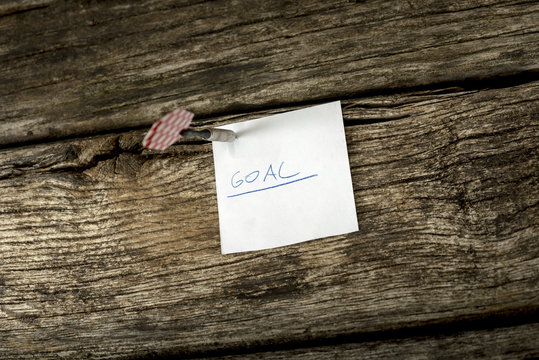White piece of paper with the word Goal pinned to a rustic woode