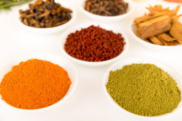 Beautiful colorful display of different spices green orange brown in white bowls, shot from above side angle, bright background