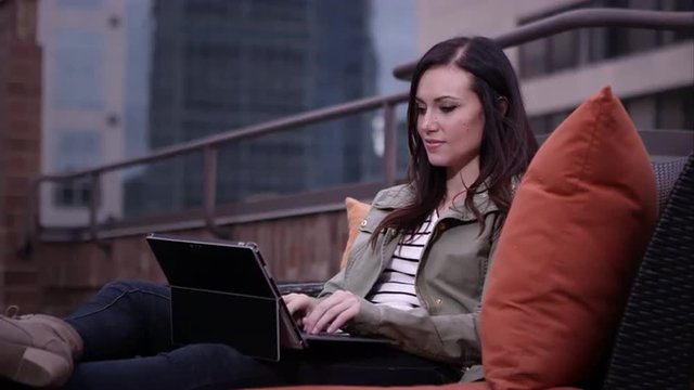 Up close view of woman relaxing on roof top typing on laptop.