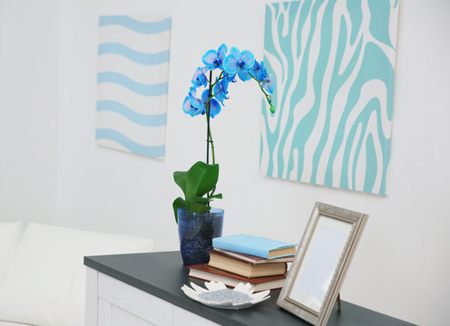 Beautiful blossoming branch of a blue orchid is on the table against wall with bright painting