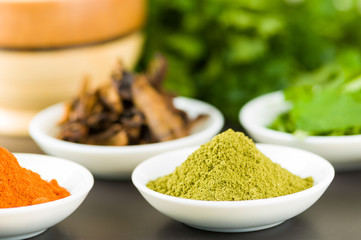Beautiful colorful display of different spices green orange brown in white bowls, shot from above side angle, grey background