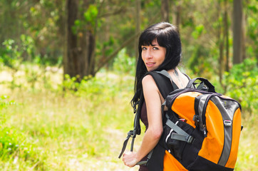 Fototapeta na wymiar Adventurous brunette in hiking environment, walking away from camera looking back, forest background