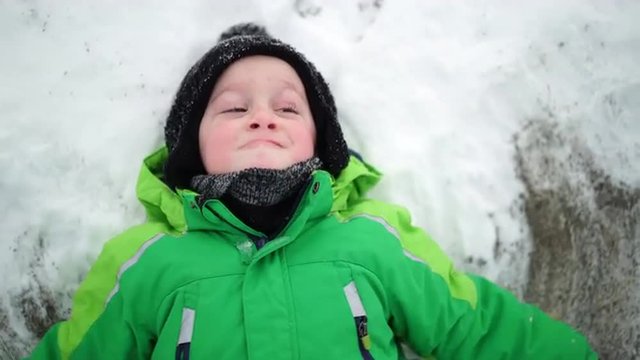 4k footage, medium shot happy little boy laying in snow trying to make an snow angel
