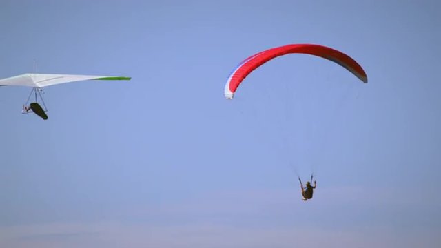 A paraglider and hang glider are flying in the same direction close to eachother.