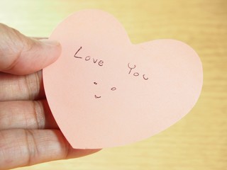 Holding pink paper, heart shape with writing ''love you'' word, Valentines day