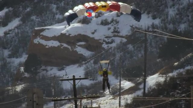 Slow motion shot of base jumper landing on snowy mountain road.