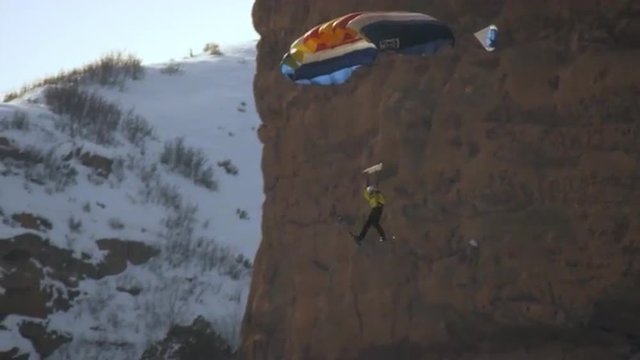 A base jumper descending a rocky mountainside in slow motion.