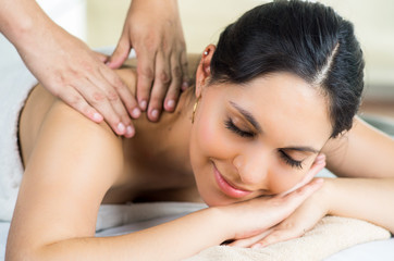 Obraz na płótnie Canvas Hispanic brunette model getting massage spa treatment, white towel covering upper body lying horizontal smiling to camera