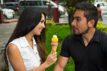 Cute hispanic couple sharing ice cream cone and enjoying each others company in outdoors environment