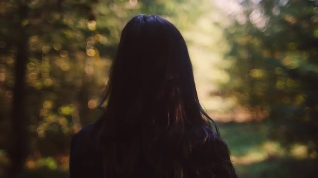 Beautiful girl in a forest walking away from the camera playing with her hair, slow motion, bokeh