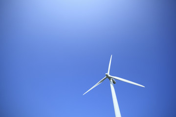 Power generating wind turbine on blue sky with sun.