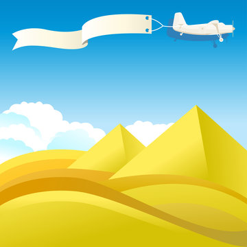 Flying vintage plane with banner and pyramids, desert landscape.