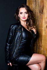 Beautiful Woman with Curly Hair dressed in black leather jacket and black dress on wooden background