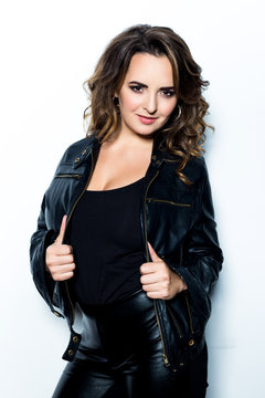 Beautiful Woman with Curly Hair dressed in black leather jacket and trousers on white background