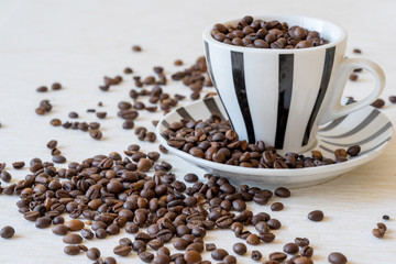 Horizontal view of coffee cup filled with coffee beans on white table.