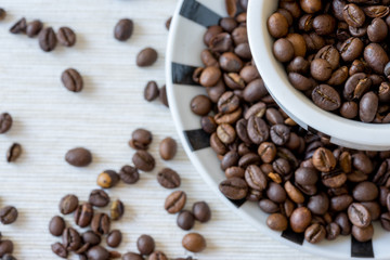 Detail view of coffee cup filled with coffee beans on white table. Selective focus.