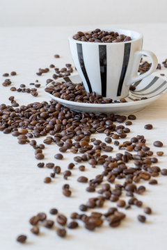 Vertical view of coffee cup filled with coffee beans on white table.