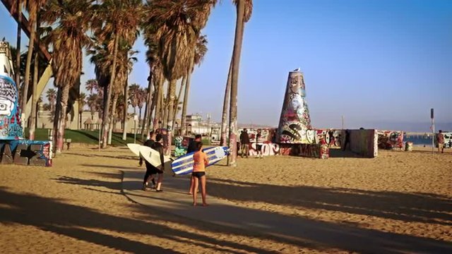 Slow motion shot of three surfers carrying surfboards walking near Venice Beach, California