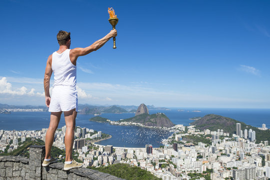 Old-fashioned athlete in classic vintage white sports uniform standing holding sport torch at city skyline overlook in Rio de Janeiro Brazil