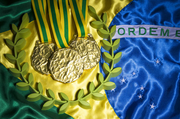 Gold medals surrounded by laurel wreath resting on shiny Brazil flag background with studio lighting