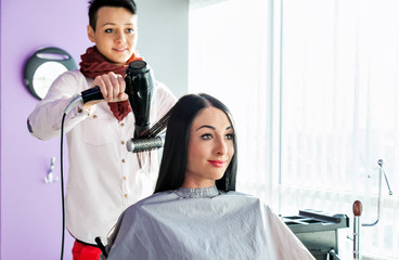  Barber with a hairdryer and comb in hand. Model with long black