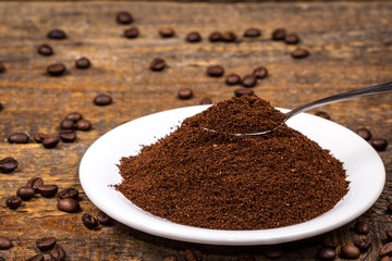 Ground coffee on white plate with sorrounding coffee beans