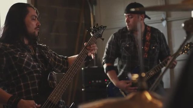 Handheld slow-motion shot of a rock band practicing in a rehearsal space.