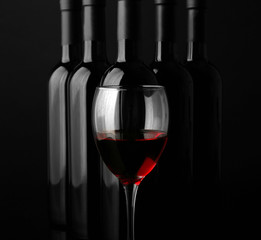 Red wine glass against bottles in a row on black background, close up