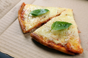 Tasty slices of pizza with basil on carton, close up