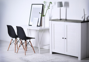 Room interior with commode, frames, chairs and table on white wall background