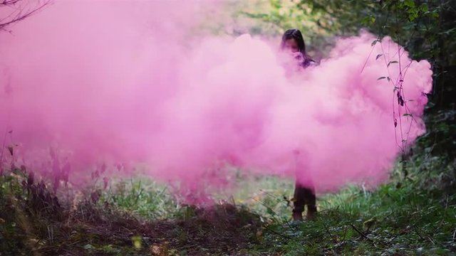 Beautiful girl in a forest runs through pink smoke from a color smoke grenade, slow motion