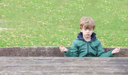 A boy is meditating on a park bench