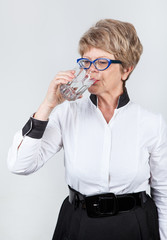 Elderly Caucasian woman drinks pure water from transparent glass, side view