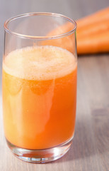 Healthy carrot smoothie in a glass and raw carrots on a wooden background