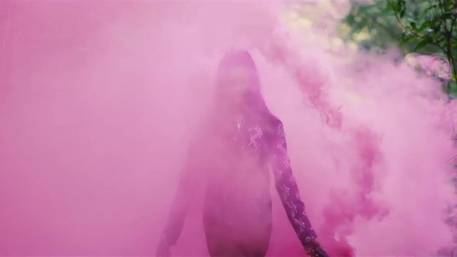 Beautiful girl in a forest waves around a pink smoke grenade and then tosses it behind her, slow motion