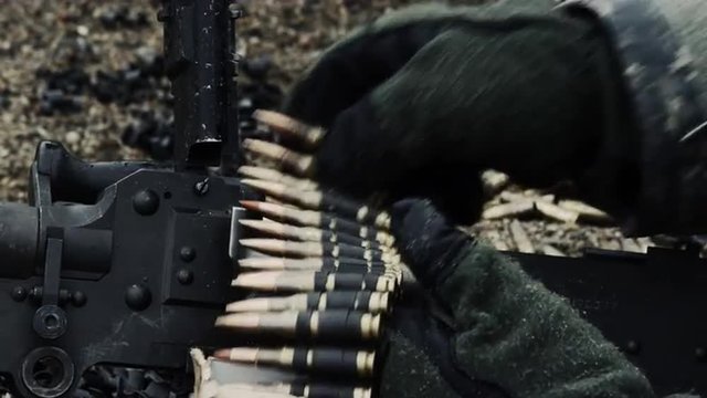 Close-up of gloved hands loading a chain of rounds.
