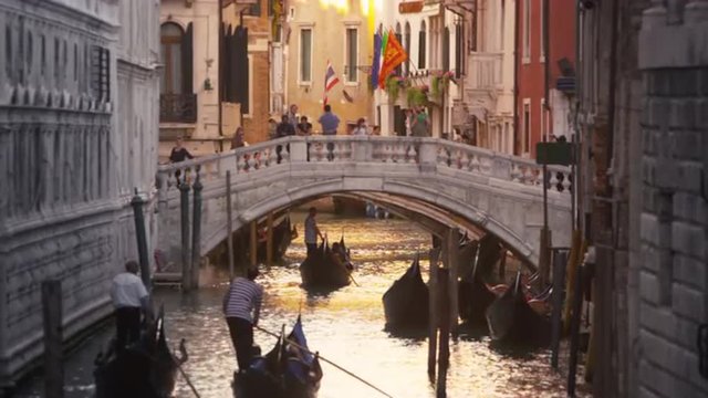 Gondolas traveling with tourists down a golden lite canal with walking bridge in Venice, Italy