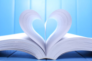Open book pages into a heart shape.On blue background.